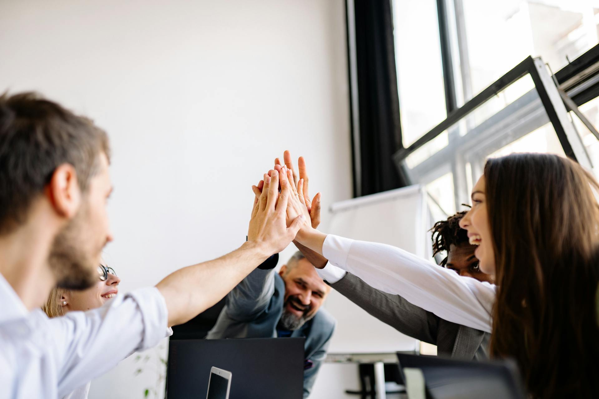 Vibrant office team sharing a group high five in a bright workspace.